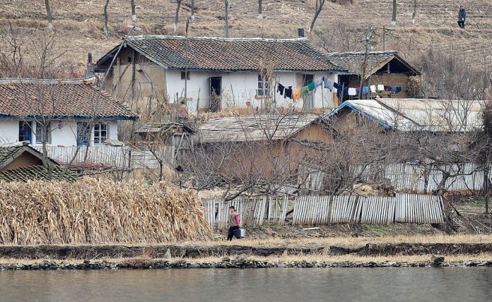 Una mujer norcoreana lleva cubos de agua fuera de casas ruinosas en medio del paisaje seco y estéril a orillas del río Yalu, situado a unos 45 kilómetros al norte de Dandong, en la provincia nororiental china de Liaoning, el 24 de noviembre de 2010. (FREDERIC J. BROWN/AFP vía Getty Images)